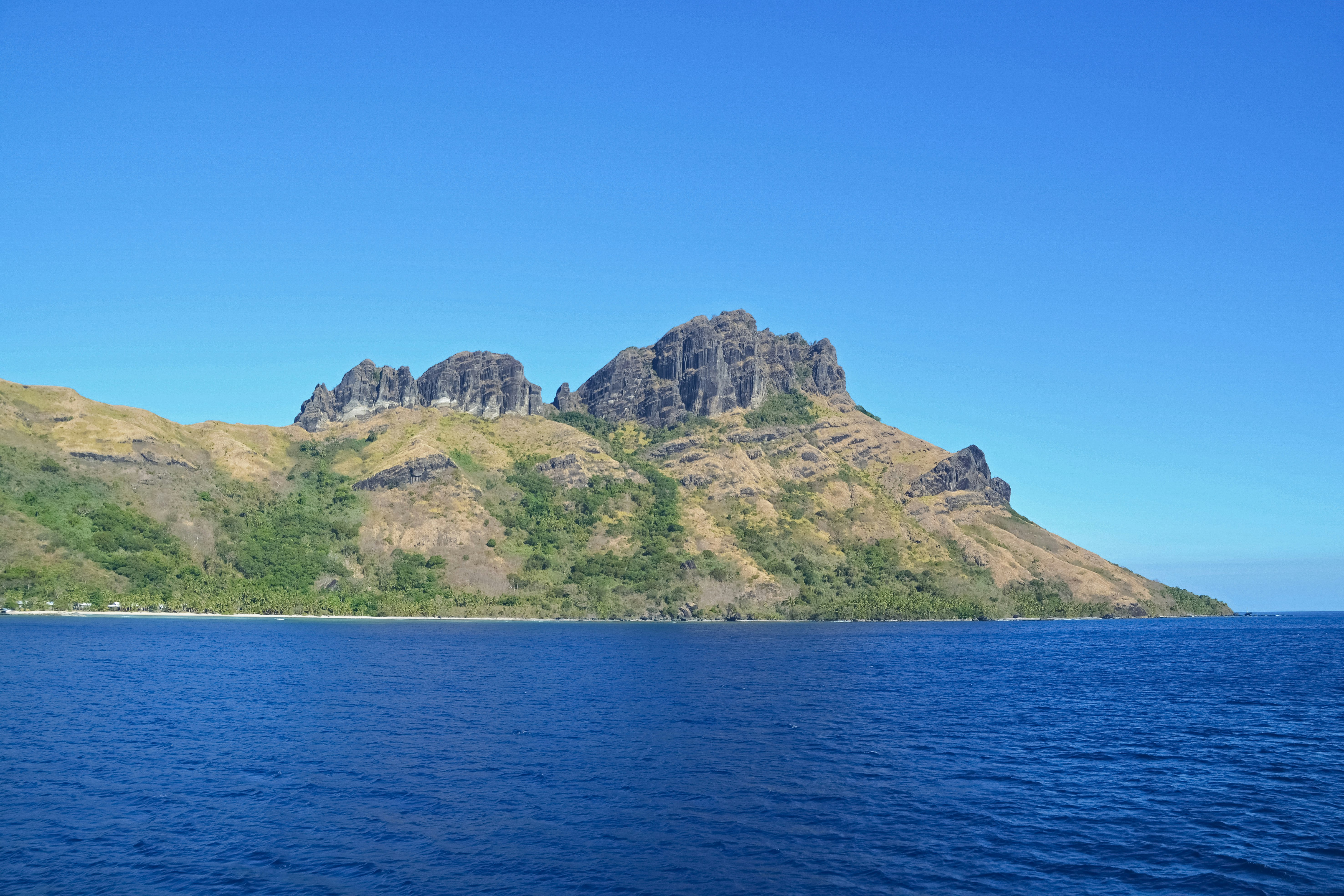 green and brown mountain beside blue sea under blue sky during daytime